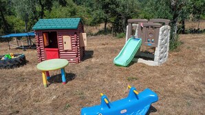 A children's play area with a small wooden house, a slide, a table, and a blue boat-shaped toy. - Casa De Campo De Oliveiras (Penela)