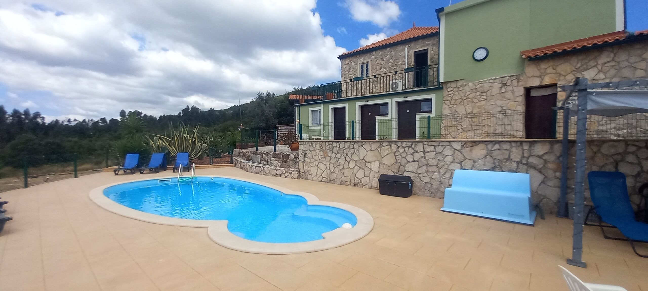 A swimming pool with lounge chairs, a stone wall, and a building with a balcony.