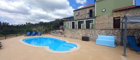 A swimming pool with lounge chairs, a stone wall, and a building with a balcony.
