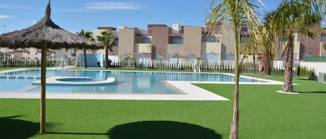 A swimming pool with a thatched umbrella, palm trees, and a well-maintained lawn.