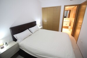 A neatly made bed with white linens, a wooden headboard, and a nightstand with a lamp. - Penthouse Aguas Nuevas Varudi Complex (Torrevieja)