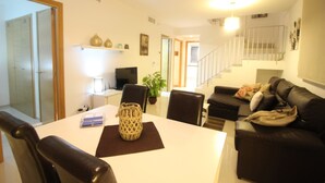 Ein modernes Wohnzimmer mit Esstisch, schwarzer Ledersofa und einer Treppe.