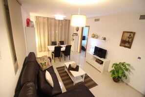 Ein modernes Wohnzimmer mit Sofa, Couchtisch, Fernseher und Essbereich.