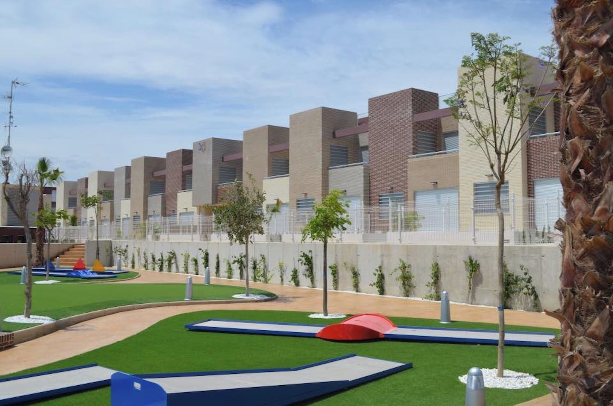 A modern building with multiple rectangular units, a green lawn area with pathways, and a palm tree.