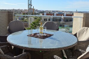 A round glass table with wicker chairs, a bottle of white wine, and glasses on a balcony overlooking a cityscape. - Penthouse Aguas Nuevas Varudi Complex (Torrevieja)