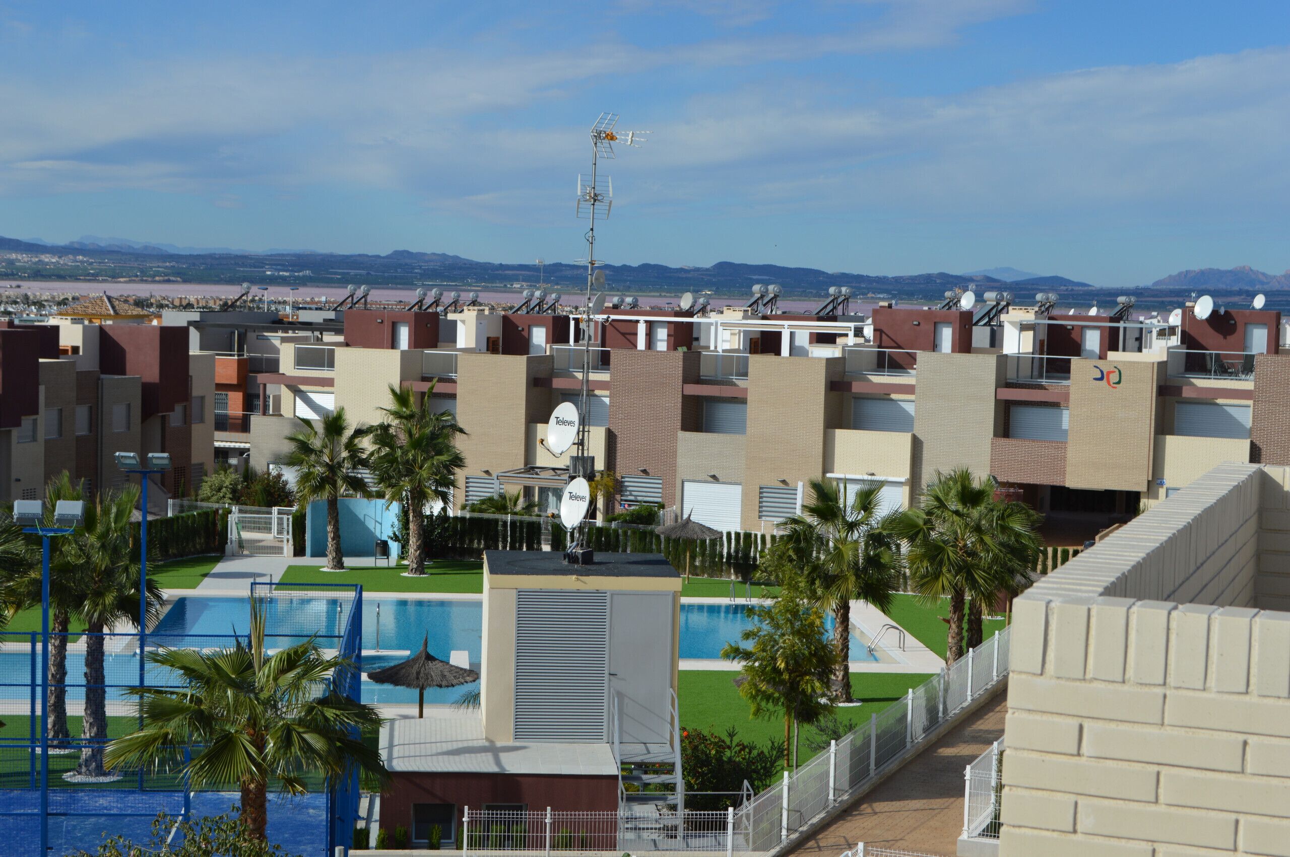 A residential complex with multiple apartment buildings, a swimming pool, and palm trees.
