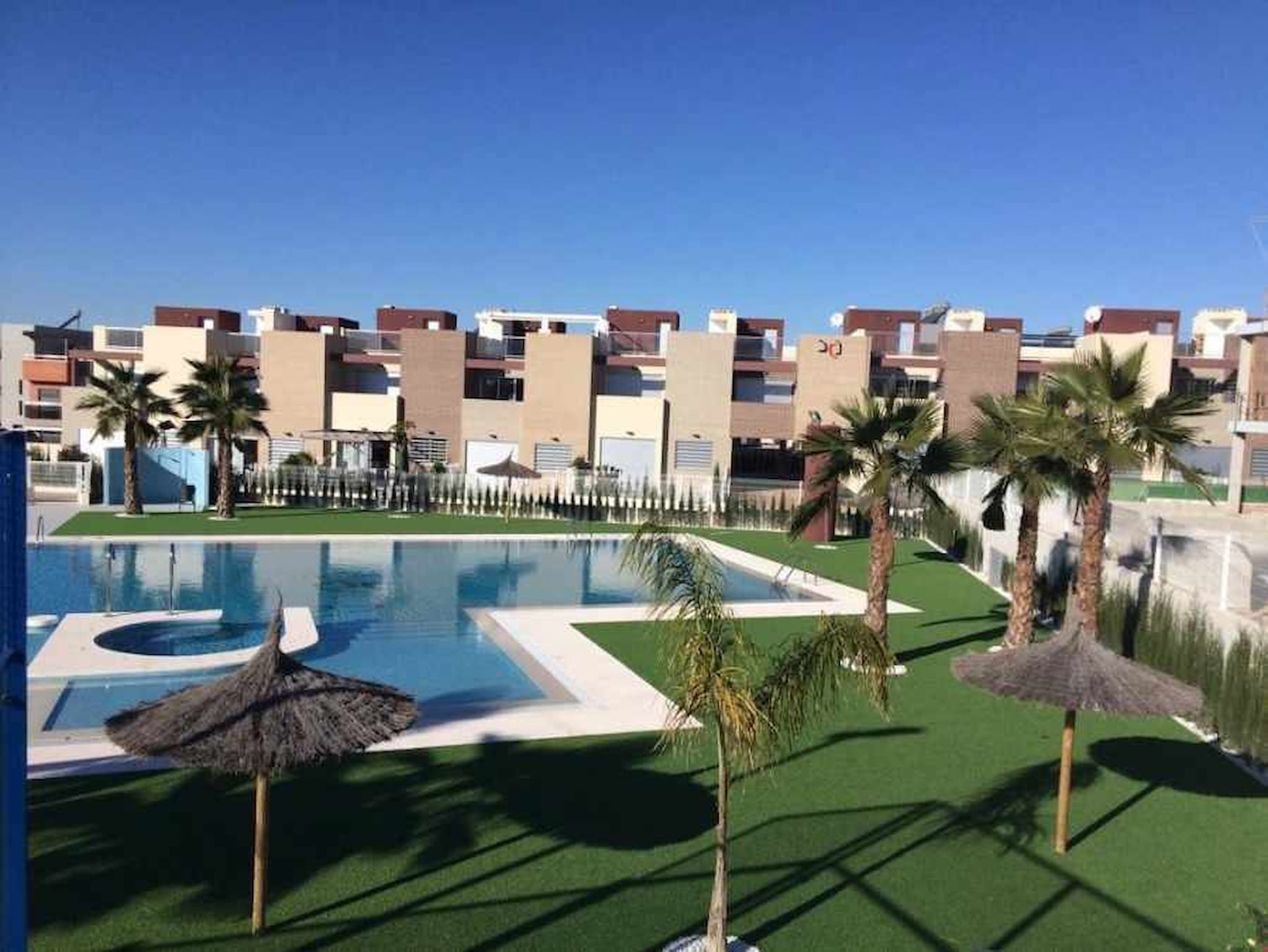 Una piscina con palme e un ombrellone di paglia, circondata da edifici moderni.