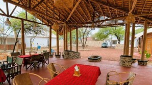 Un área de comedor al aire libre con techo de paja, mesas con manteles a cuadros rojos y sillas de mimbre.