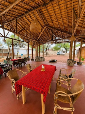 Un área de comedor al aire libre con techo de paja, mesas con manteles a cuadros rojos y sillas de mimbre.