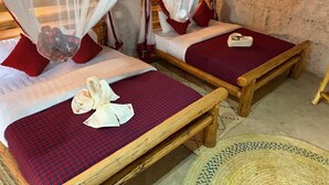 Dos camas de madera con ropa de cama roja y blanca, un tapete tejido y una mesita.