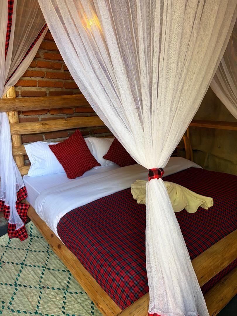 Uma cama com dossel, roupa de cama vermelha e branca, e um cobertor xadrez.