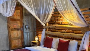 Una cama de madera con dosel, ropa de cama roja y blanca, y una pared de ladrillo rústico.