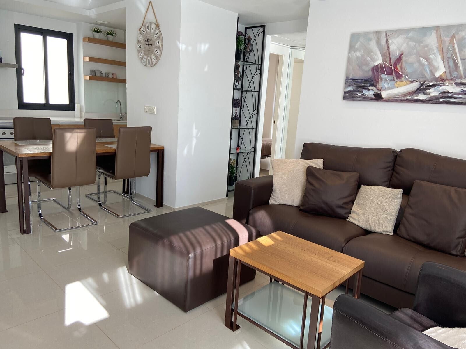 Una sala moderna con un sofá de cuero marrón, una mesa de centro de vidrio y un comedor con mesa y sillas de madera.