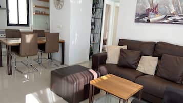 Una sala moderna con un sofá de cuero marrón, una mesa de centro de vidrio y un comedor con mesa y sillas de madera.
