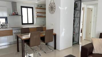 A modern kitchen with a dining area, a living room with a sofa, and a decorative wall clock.