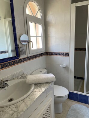 Un baño con lavamanos de mármol, inodoro y ducha.