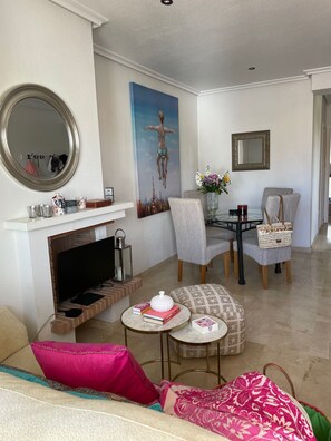 A living room with a fireplace, a dining area with chairs and a table, a large mirror, and a painting on the wall. - Penthouse Villamartin Laplaza Destino (Orihuela)