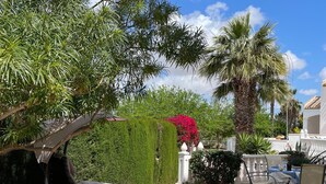 A patio area with a round table, chairs, a hanging chair, a small fountain, and a variety of plants and trees. - Penthouse Villamartin Laplaza Destino (Orihuela)