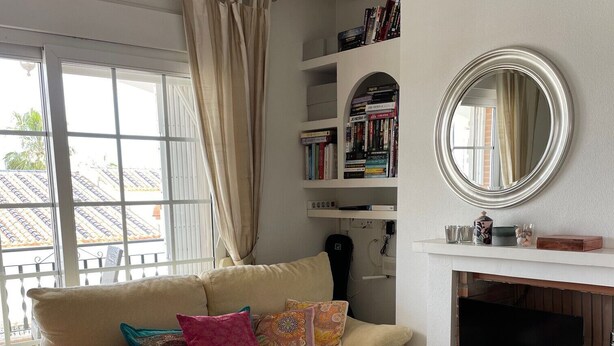 A living room with a sofa, a coffee table, a fireplace, a bookshelf, and a large window with curtains. - Penthouse Villamartin Laplaza Destino (Orihuela)
