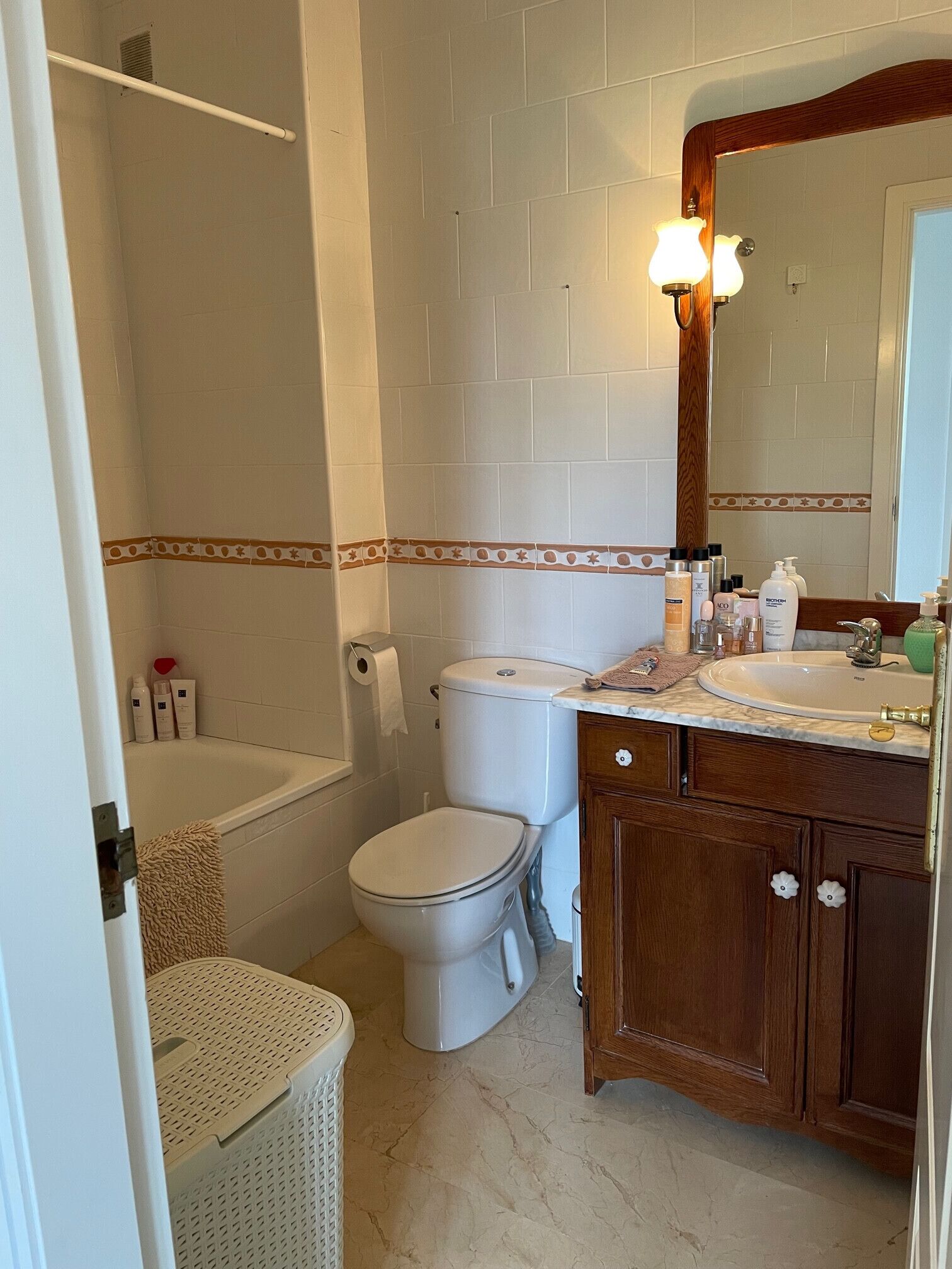 Un baño con inodoro, lavamanos y bañera. Hay artículos de aseo en la encimera.