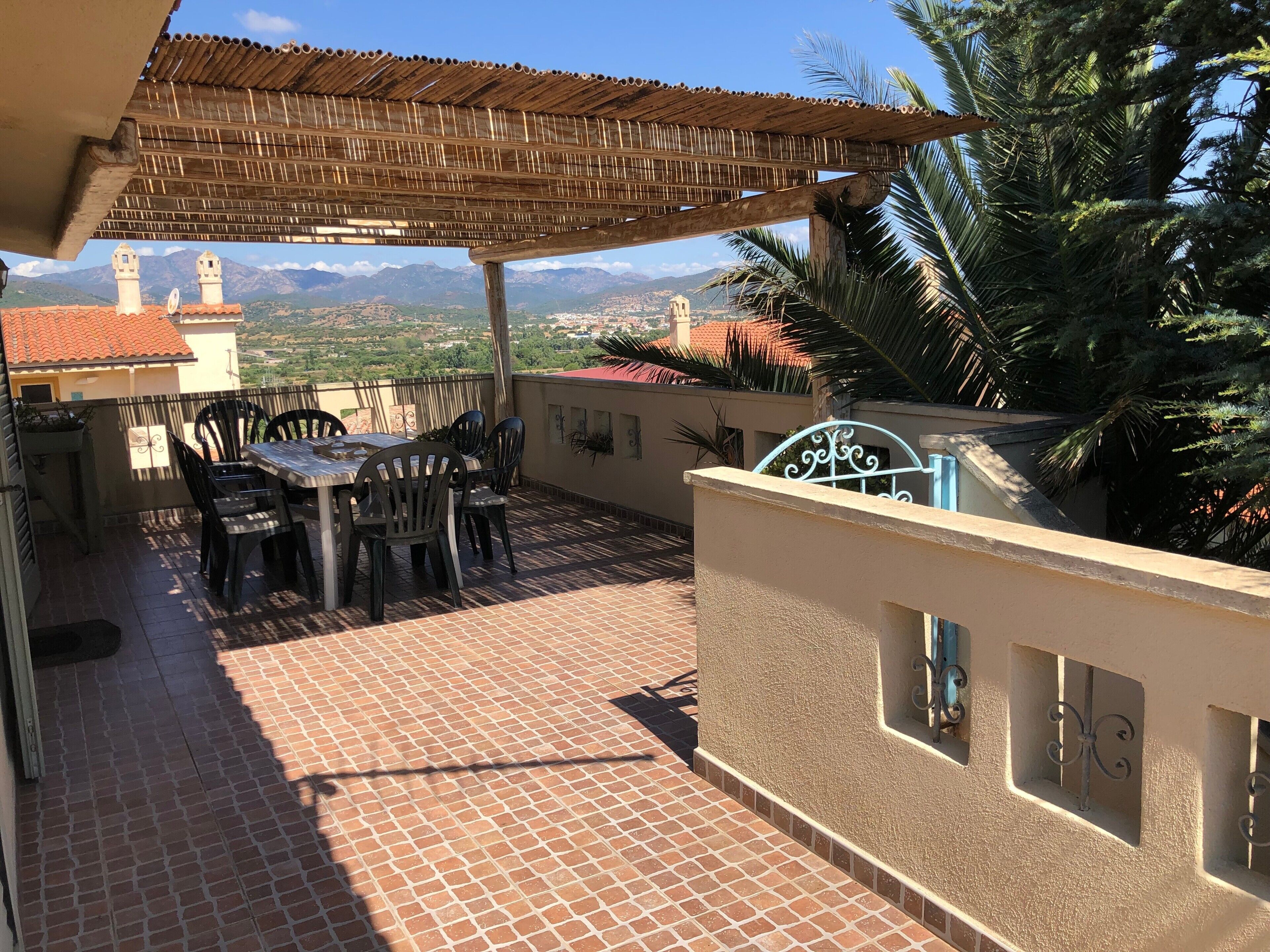 Een terras met een tafel, stoelen, een pergola en uitzicht op verre bergen.