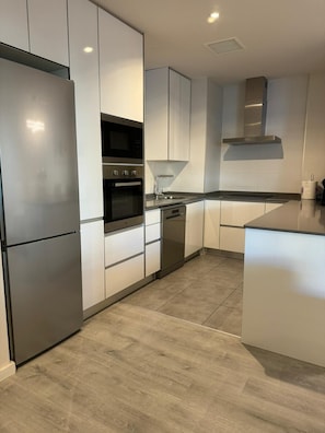 Una cocina moderna con electrodomésticos de acero inoxidable, armarios blancos y piso de madera.