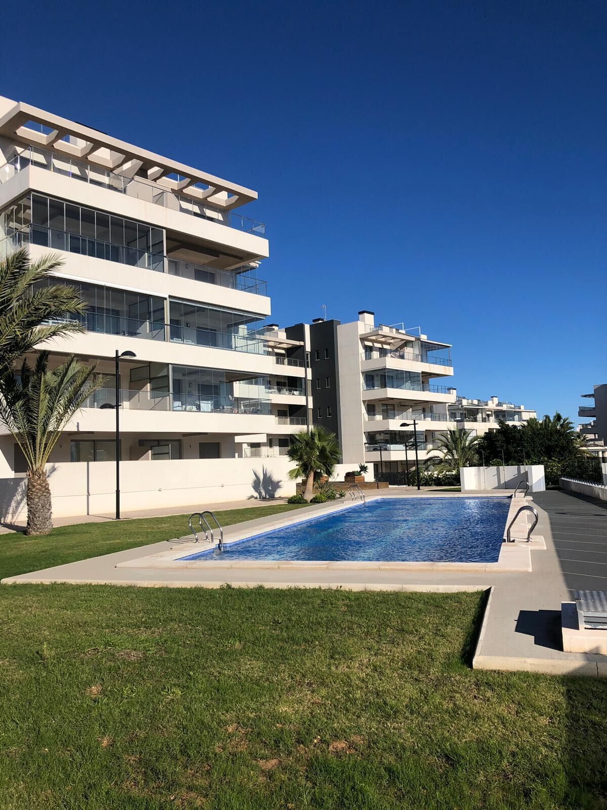 A modern apartment building with a swimming pool, balconies, and a clear blue sky.