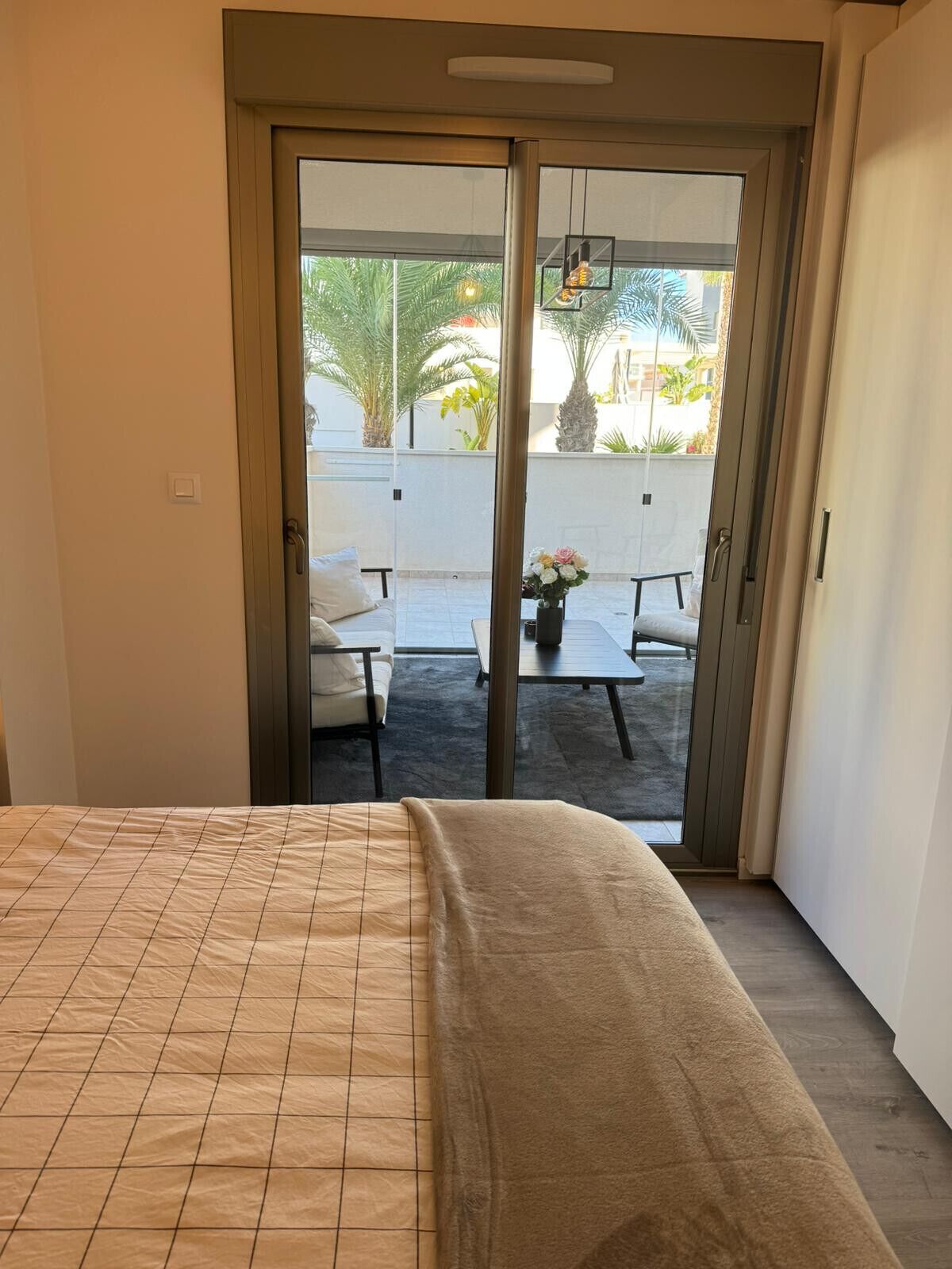 A bedroom with a bed, a sliding glass door leading to an outdoor patio with a table and chairs.
