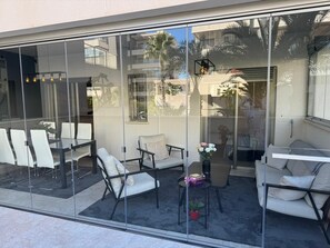 Un espacio moderno al aire libre con paredes de vidrio, sillas blancas y una pequeña mesa con flores.