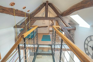 Eine Holztreppe mit Glaseinlage führt zu einem Schlafzimmer im oberen Bereich, das ein Dachfenster und eine große Wanduhr hat.