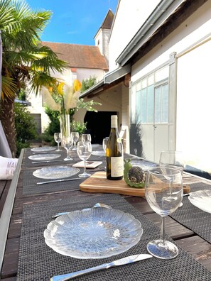 An outdoor dining area with a table set for four, including wine glasses, plates, and cutlery. - Vrbo Property (Morey-Saint-Denis)