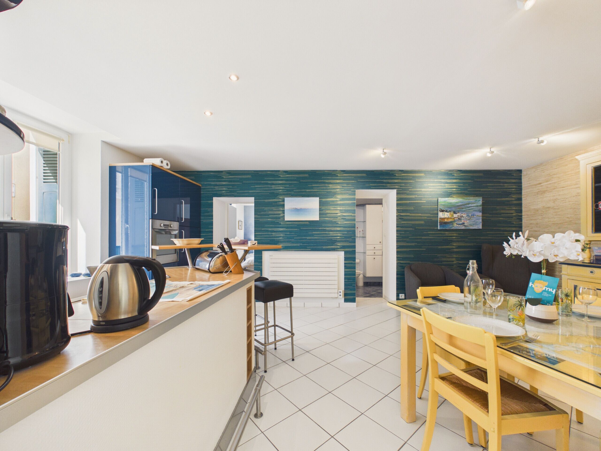 Una cocina moderna con una isla central, un comedor con mesa de vidrio y una sala de estar con sofá y mesa de centro.