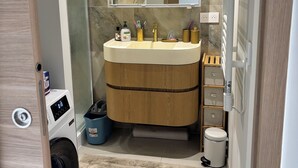 Ein modernes Badezimmer mit Marmor-Spritzschutz, einem Holz-Waschtisch und einer Waschmaschine, die in den Schrank integriert ist, sowie einem Spiegel über dem Waschbecken.