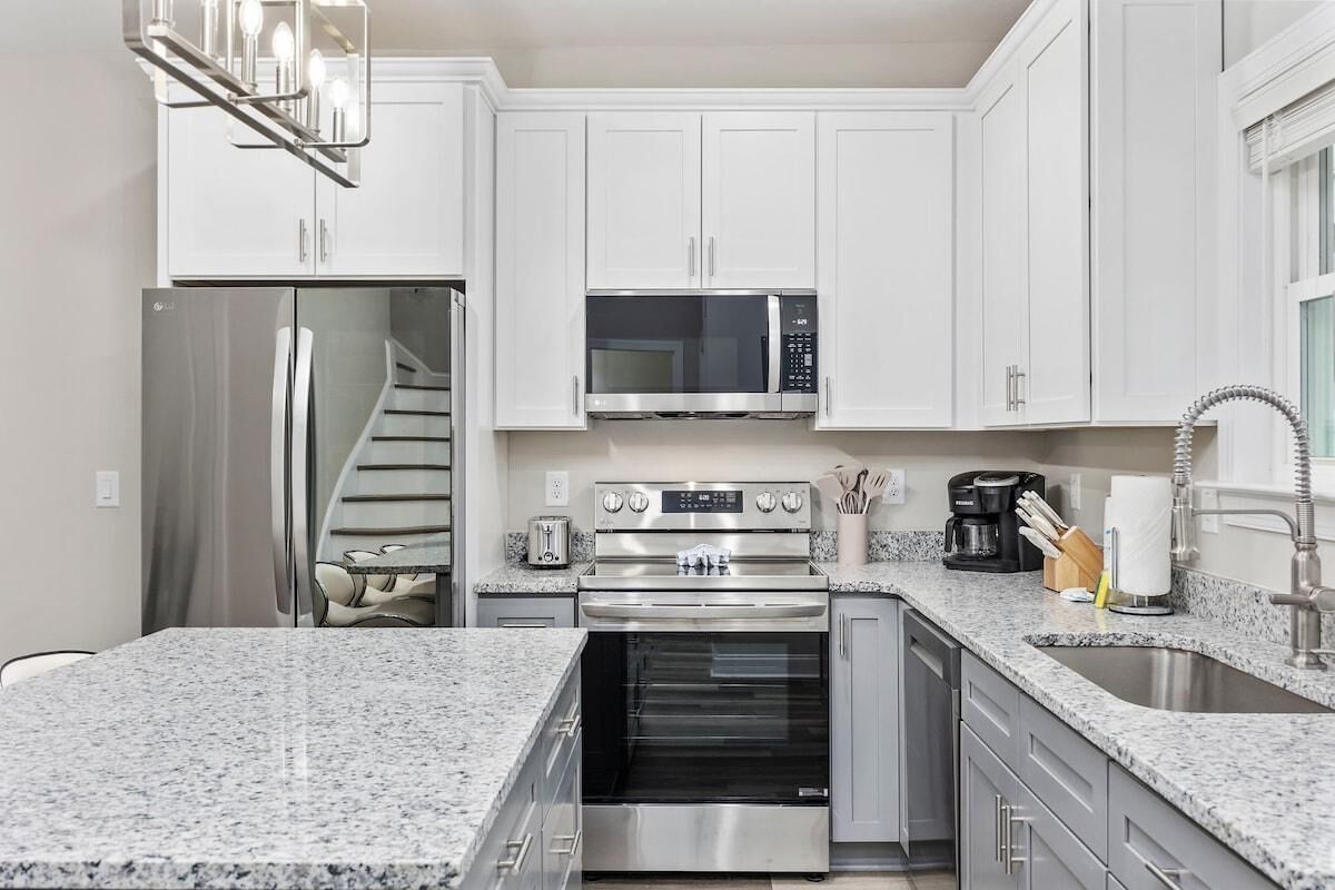 A modern kitchen with white cabinets, stainless steel appliances, granite countertops, and a built-in oven.