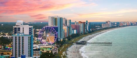A coastal cityscape with high-rise buildings, a beach, and a Ferris wheel.