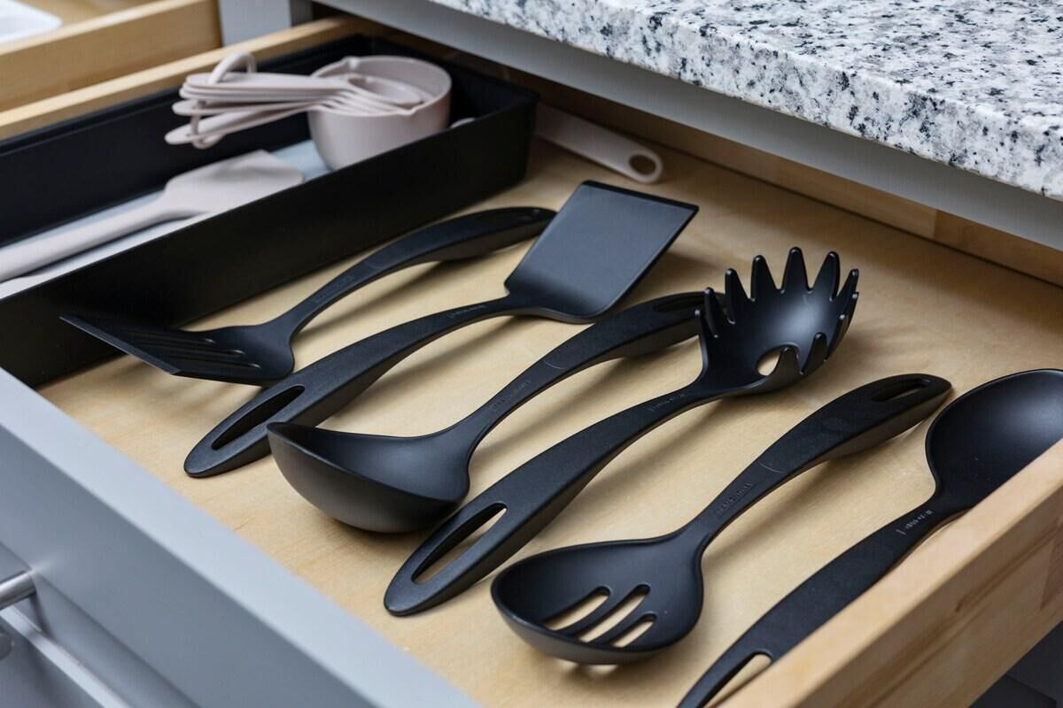 Un cassetto pieno di vari utensili da cucina neri, tra cui una spatola, un mestolo forato e un cucchiaio.