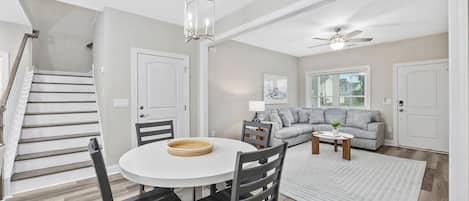 A spacious living area with a staircase, a round dining table, and a grey sofa.