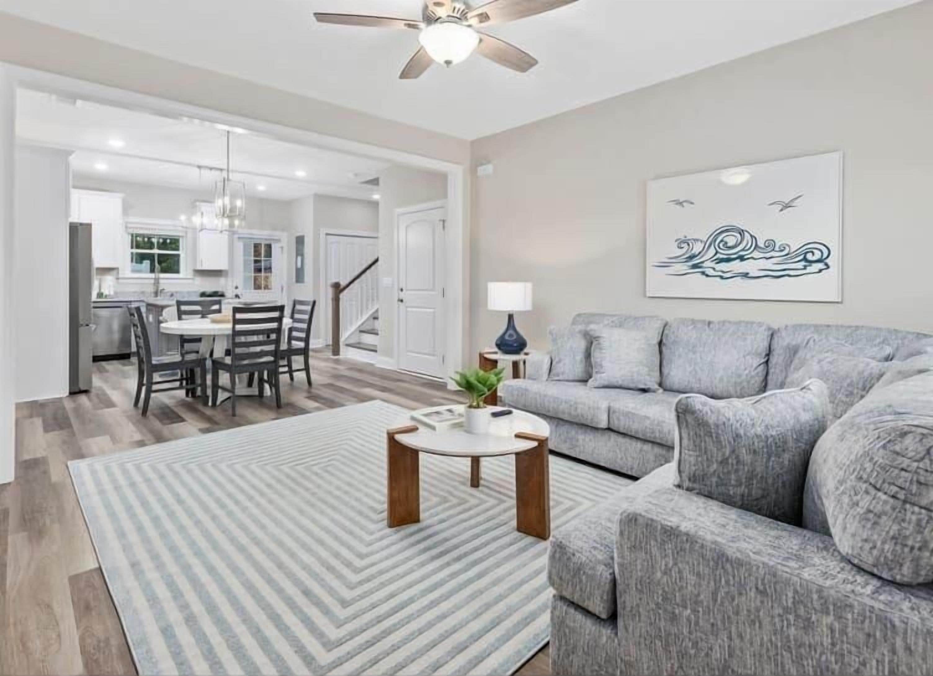 A modern living room with a grey sofa, a striped rug, and a ceiling fan.