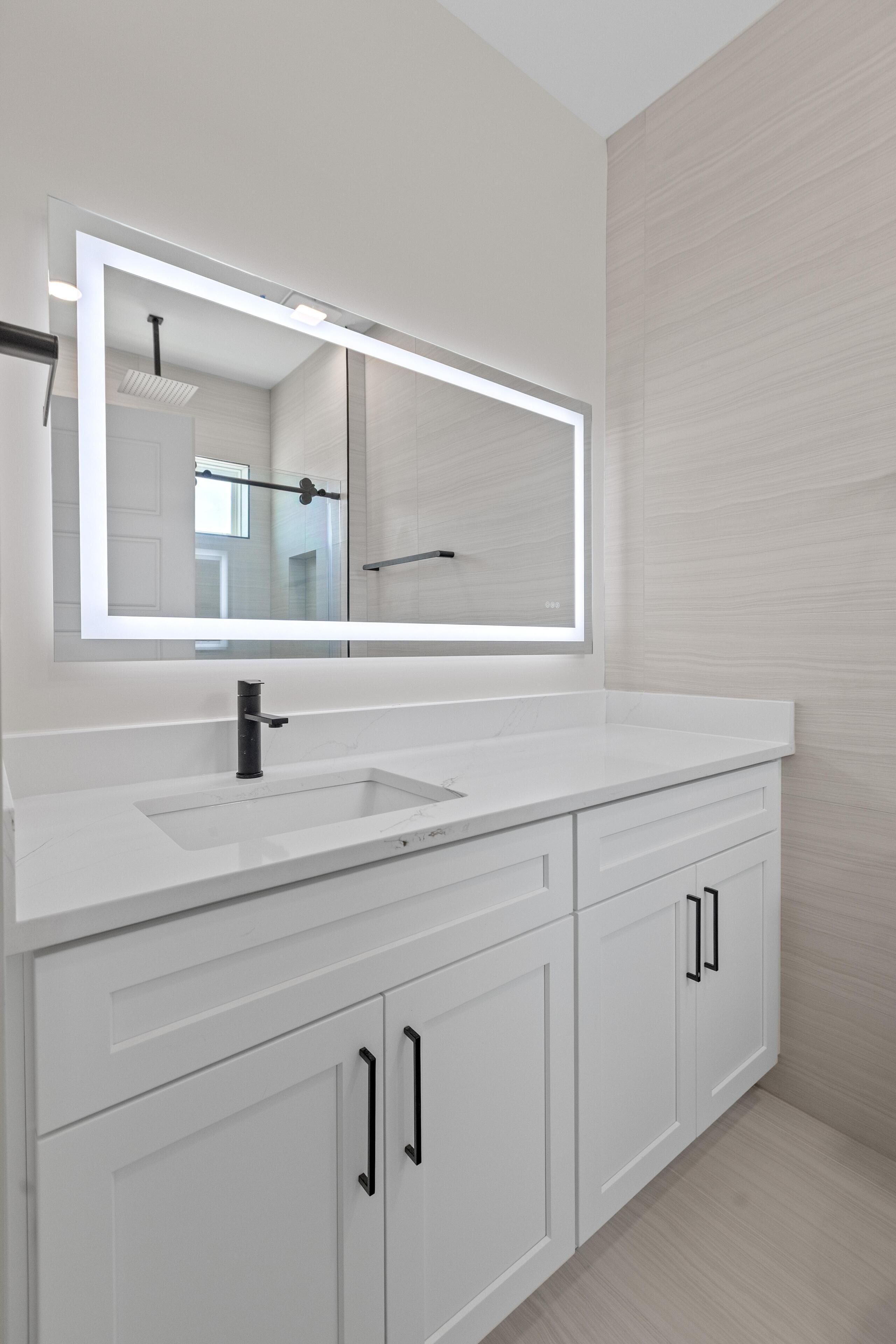 A modern bathroom with a large mirror, white vanity, and cabinets.