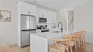 A modern kitchen with white cabinetry, stainless steel appliances, a central island with bar stools, and a staircase leading to another level. - Beachwalk Club Steps to Beach Sleeps 16 Pets (Myrtle Beach)