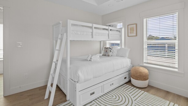 A bunk bed with a ladder, a bedside table, a window with blinds, and a patterned rug. - Beachwalk Club Steps to Beach Sleeps 16 Pets (Myrtle Beach)