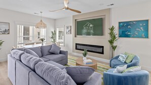 A modern living room with a grey sectional sofa, a blue armchair, a wooden coffee table, and a ceiling fan. - Beachwalk Club Steps to Beach Sleeps 16 Pets (Myrtle Beach)