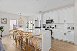 Cocina moderna con armarios blancos, una isla central con taburetes, electrodomésticos de acero inoxidable y un ventanal grande.