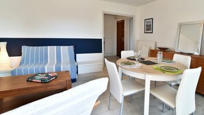 A modern living room with a sofa, a dining table set for four, and a large mirror. - Le Balcon d'Émeraude - À moins d’1 km de la plage (Dinard)
