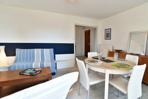 Ein modernes Wohnzimmer mit einer Couch, einem Esstisch für vier Personen und einem großen Spiegel.