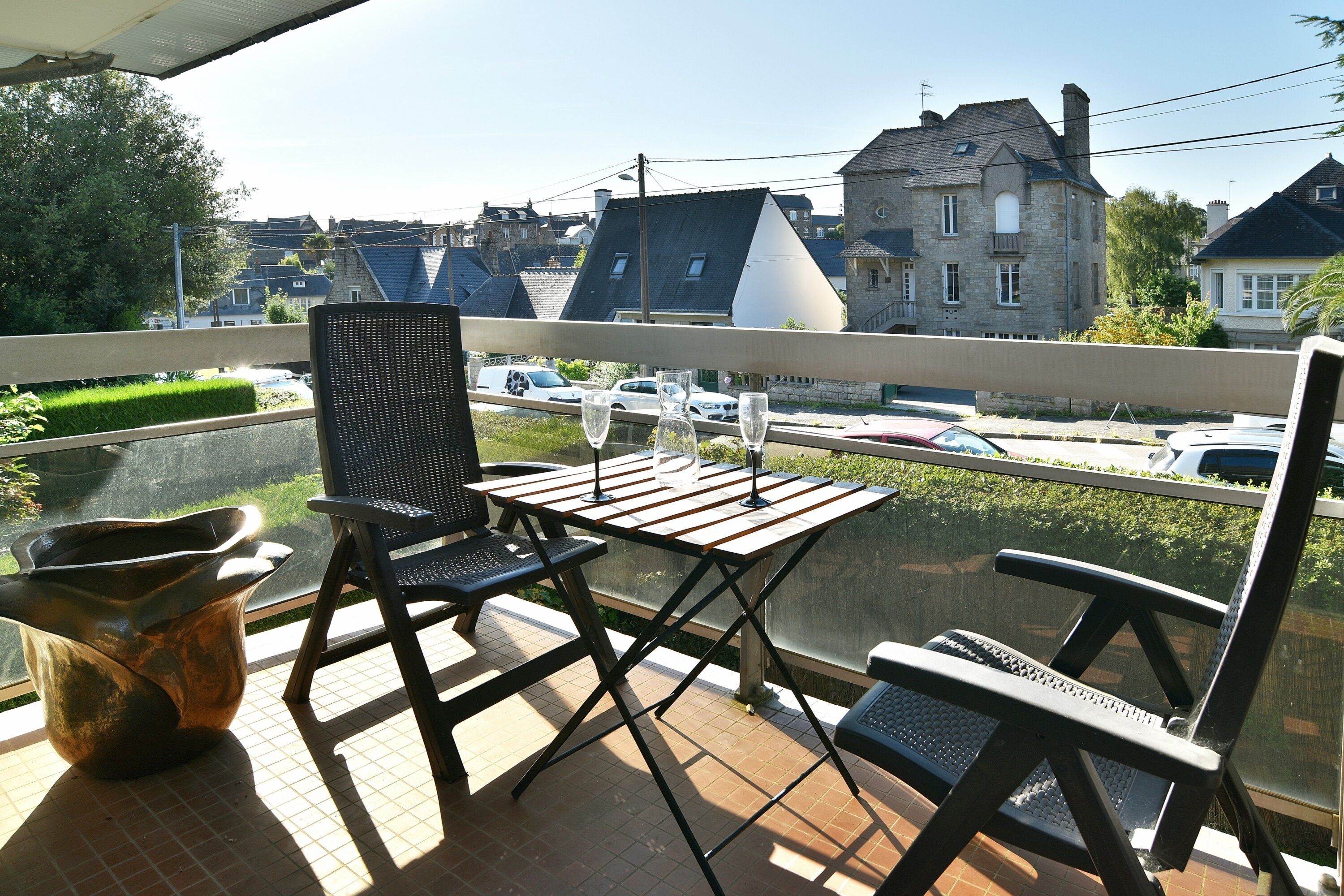 Un balcon avec une table et des chaises, un pot de fleurs et une vue sur la rue et les immeubles.