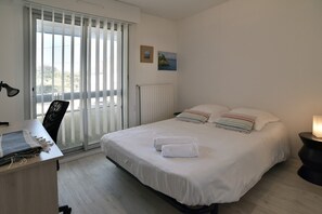 Ein Schlafzimmer mit Bett, Schreibtisch, Stuhl, Heizkörper und einem Fenster mit Jalousien.