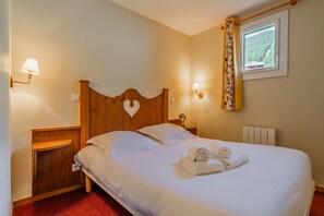 Ein ordentlich bezogenes Bett mit weißen Leinen und aufgerollten Handtüchern, ein Holz-Kopfteil, Nachttischlampen und ein Fenster mit Blick auf Grünflächen.