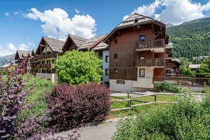 Ein Chalet-Hotel aus Holz mit Balkonen, umgeben von üppiger Vegetation und Bergen im Hintergrund.