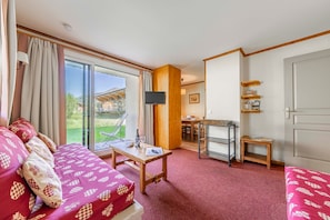 Ein Hotelzimmer mit einer rot gemusterten Couch, einem Holztisch, einem Fernseher und einer Glastür, die auf einen Balkon führt.